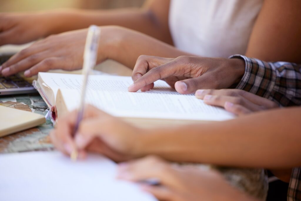 Students, education and hands writing in notebook for learning, exam studying and write notes in cl